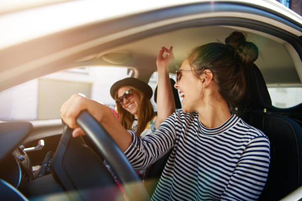 Two young women having fun driving along a street Two young women having fun driving along the street laughing and joking with the driver distracted looking at her passenger karaoke photos stock pictures, royalty-free photos & images