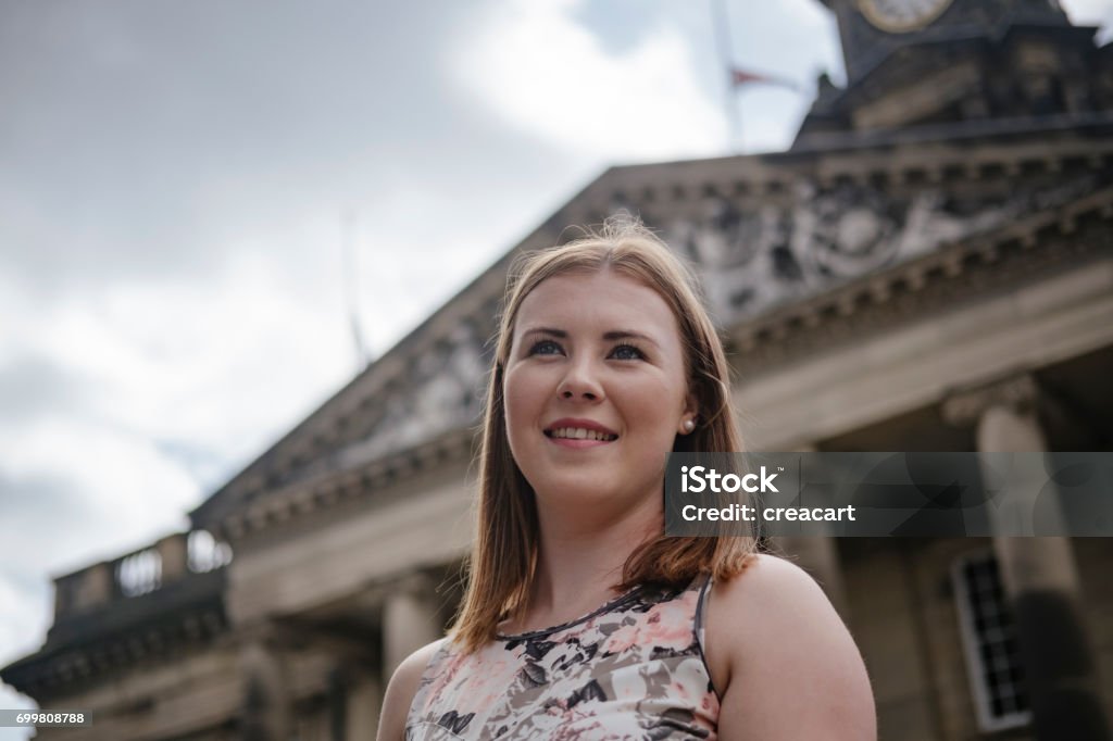 Candid street Portrait of a young woman in a UK City. Candid summer day Street Portrait of a pretty young woman in a summer dress de-focused streets and building of Lancaster as a backdrop. Lancaster - Lancashire Stock Photo