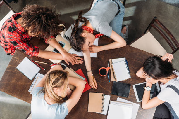 istock Overhead view of tired young students sleeping on table with notebooks and digital devices 699822400