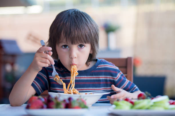 mignon enfant, garçon d’âge préscolaire, manger des spaghettis pour déjeuner à l’extérieur - child eating pasta spaghetti photos et images de collection
