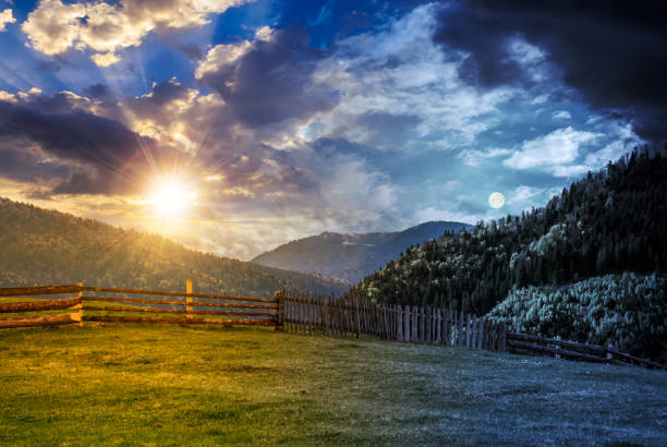 fence through the grassy meadow in mountains time change concept day and night time change concept. wooden fence through the grassy meadow in mountains. beautiful Carpathian countryside landscape with cloudy sky with sun and moon day and night stock pictures, royalty-free photos & images