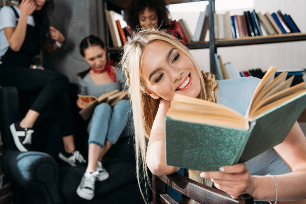 istock caucasian girl reading book while her friends sitting on sofa at home library 699853682