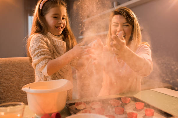istock Joyful little girl and her mother having fun with flour while making a cake. 699856934