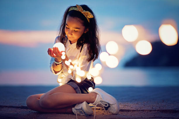 niña está sentado en el muelle y jugando con las luces misteriosas - fairy child outdoors fairy tale fotografías e imágenes de stock