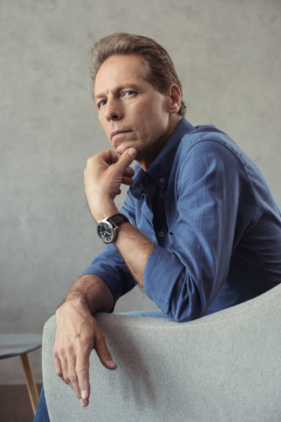 istock mature man sitting on armchair in thoughtful pose and looking at camera 699868564