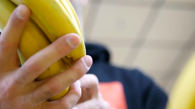 Male hand selecting bananas at the supermarket. Man taking a bunch of bananas from counter in a grocery store. Guy selecting fresh fruit at produce department of shop. Buyer chooses food. Close up