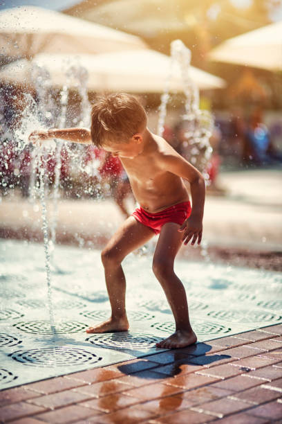 istock Little boy playing in splash pool fountains. 699880284