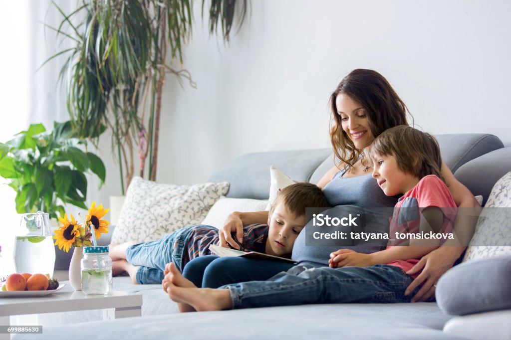 Young pregnant woman, reading book at home to her boys Young pregnant woman, reading a book at home to her two boys, eating fruits, hugging and laughing Pregnant Stock Photo