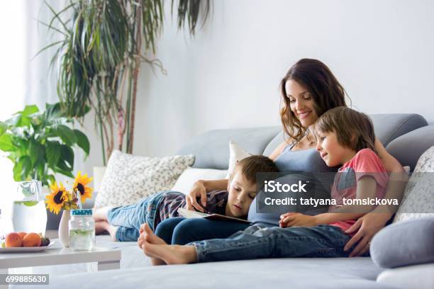 Young Pregnant Woman Reading Book At Home To Her Boys Stock Photo - Download Image Now