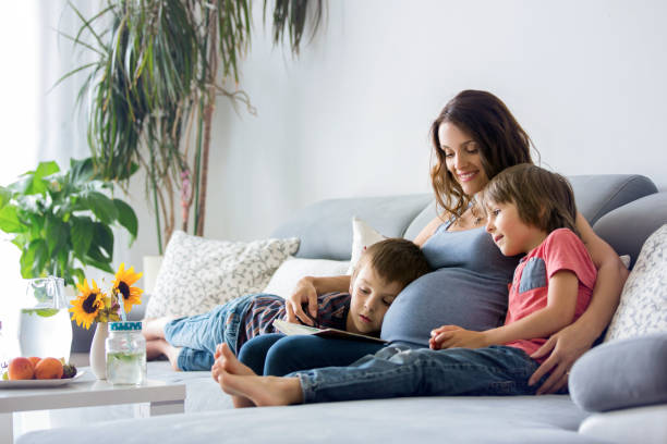 young pregnant woman, reading book at home to her boys - relaxation exercise child mother human pregnancy imagens e fotografias de stock