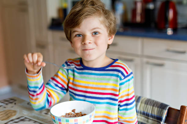 garoto loiro menino feliz comendo cereais para pequeno-almoço ou almoço. uma alimentação saudável para crianças. - little boys breakfast caucasian child - fotografias e filmes do acervo
