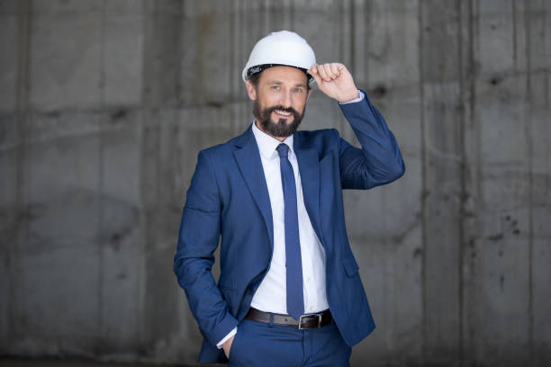 istock Handsome middle aged businessman in hard hat and suit standing and smiling at work 699937912