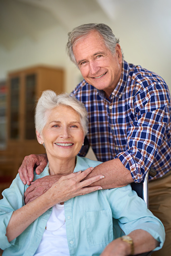 Portrait of a happy senior woman in a wheelchair posing with her husband at home