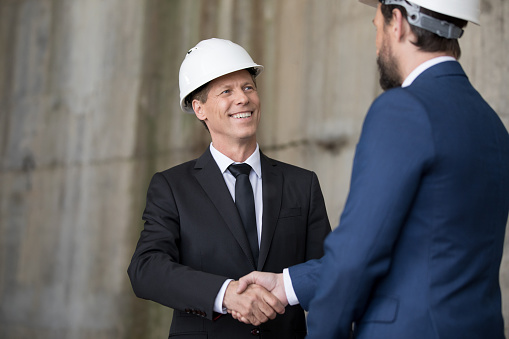 Two professional engineers in hard hats shaking hands and looking at each other