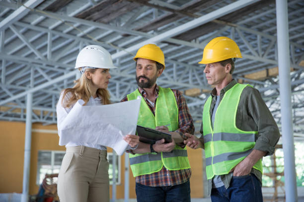 istock Serious inspector holding blueprint and looking at workers in hard hats 699946216