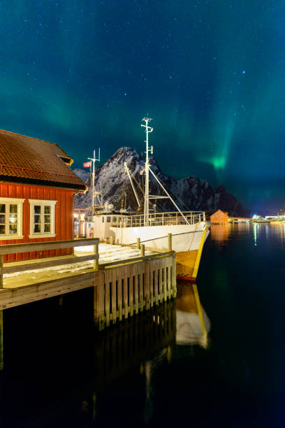 Northern lights over the harbor of Svolvaer in the Lofoten, Norway Northern Lights, polar light or Aurora Borealis in the night sky over the port of Svolvaer in the Lofoten in Nordland Norway. A fishing boat is moored in front of a cabin. harbor of svolvaer in winter lofoten islands norway stock pictures, royalty-free photos & images
