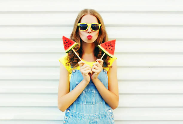 ziemlich coole mädchenmode mit ein zwei stück wassermelone eis weht ihre lippen über einen weißen hintergrund - fruit flavor stock-fotos und bilder