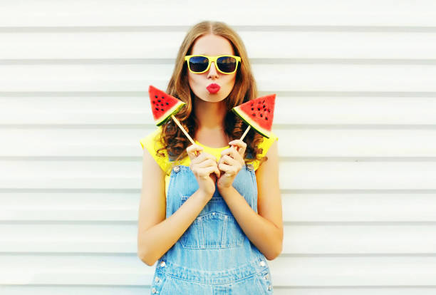 мода довольно прохладно девушка с двумя ломтиками арбузного мороженого дует губы на белом фоне - fruit flavor стоковые фото и изображения