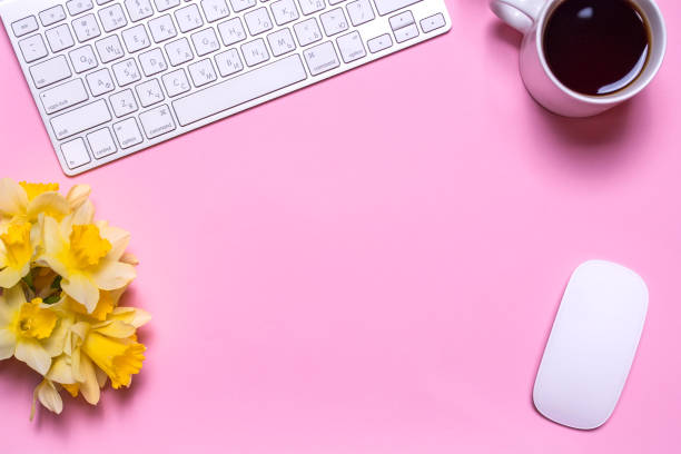 istock Office workplace with keyboard, a daffodils, a cup of tea and PC mouse on a pink background. 700069910