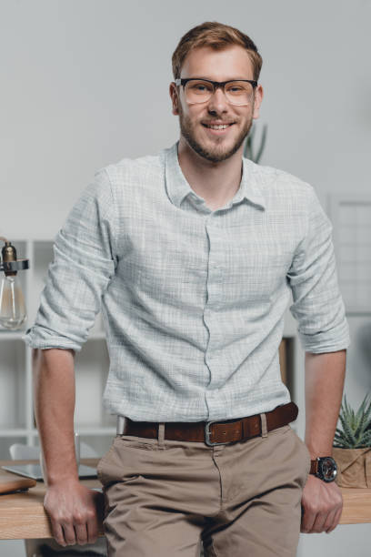 istock happy caucasian businessman looking at camera and leaning on table in modern office 700100758