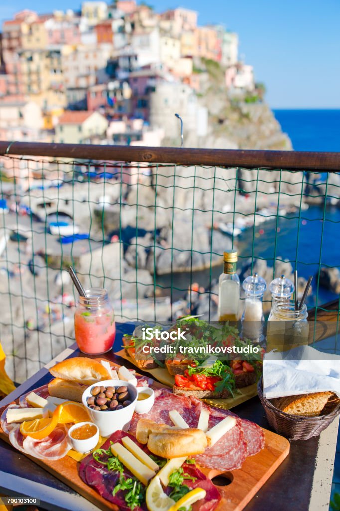 Tasty italian snacks. Fresh bruschettes, cheeses and meat on the board in outdoor cafe with amazing view in Manarola, Italy Tasty italian snack. Fresh bruschettes, cheeses and meat on the board in outdoor cafe with amazing view in Manarola Aperitif Stock Photo