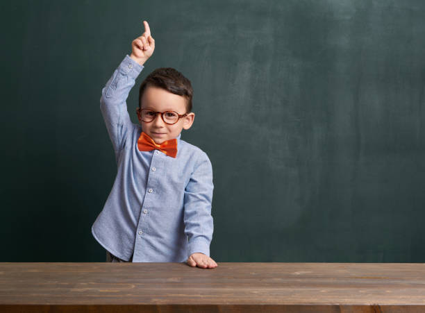 istock Cute child is in front of chalkboard and raising hand 700105238