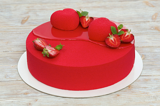 Red velvet cake partly covered with red mirror glaze, decorated with strawberry, mint and red hearts. Closeup view.