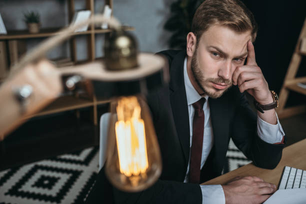 istock pensive caucasian businessman in suit looking at lamp while sitting at workplace 700109716