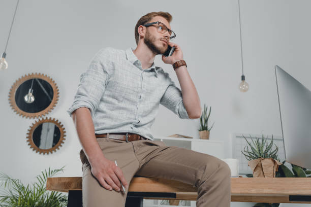 istock serious caucasian businessman using smartphone and leaning on table in modern office 700110772