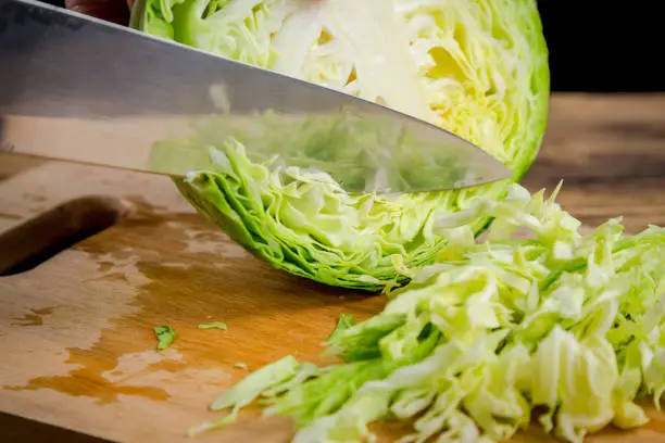 Slicing cabbage with kitchen knife on wooden board, isolated on black background
