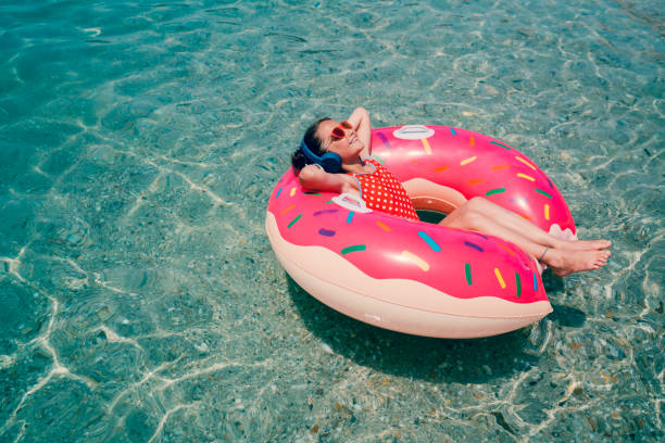 Little girl sunbathing in life preserver Smiling girl floating on water and listening to the music girls laying on beach stock pictures, royalty-free photos & images