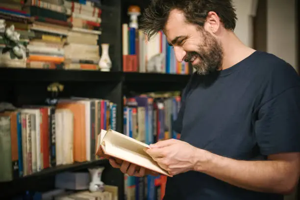 Curious man choosing book in his library at home. Close up