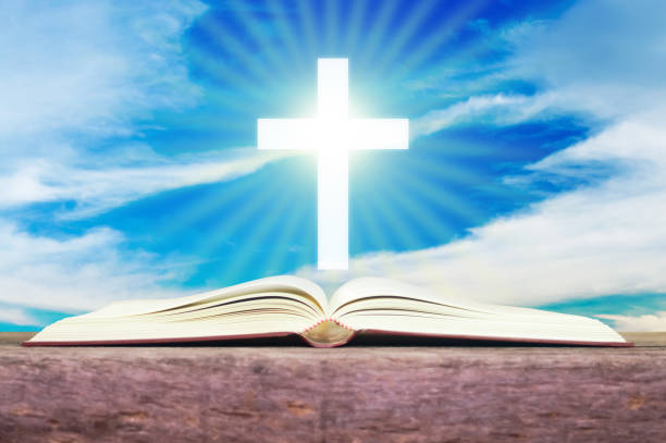 istock Open holy bible with white cross in the blue sky back ground. 700194866