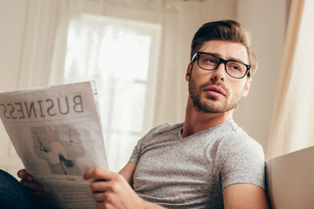 istock young handsome man in glasses reading newspaper while sitting at home 700195280