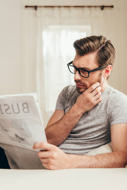 istock handsome man in glasses reading newspaper in thoughtful pose at home 700197134