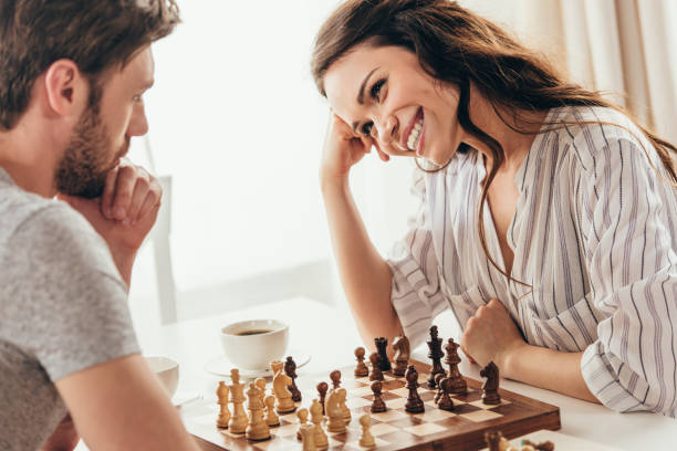 pareja joven jugando al ajedrez mientras estaba sentado en la mesa en casa - juego de ajedrez fotografías e imágenes de stock