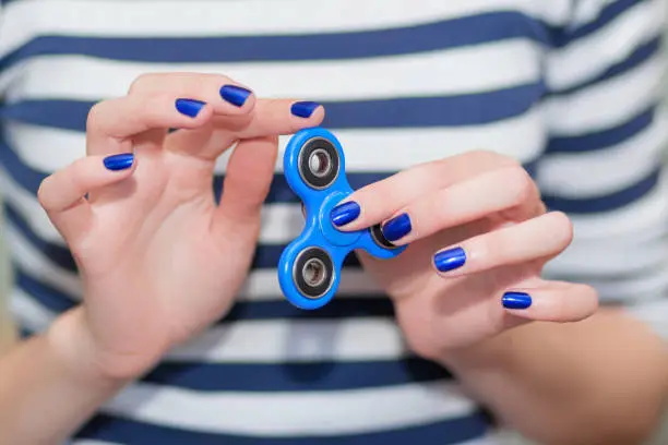 Photo of A girl is holding a popular toy fidget spinner in her hands. Stress relief. Anti stress and relaxation fidgets, spinner for tired people. Girl playing with a fidget spinner.