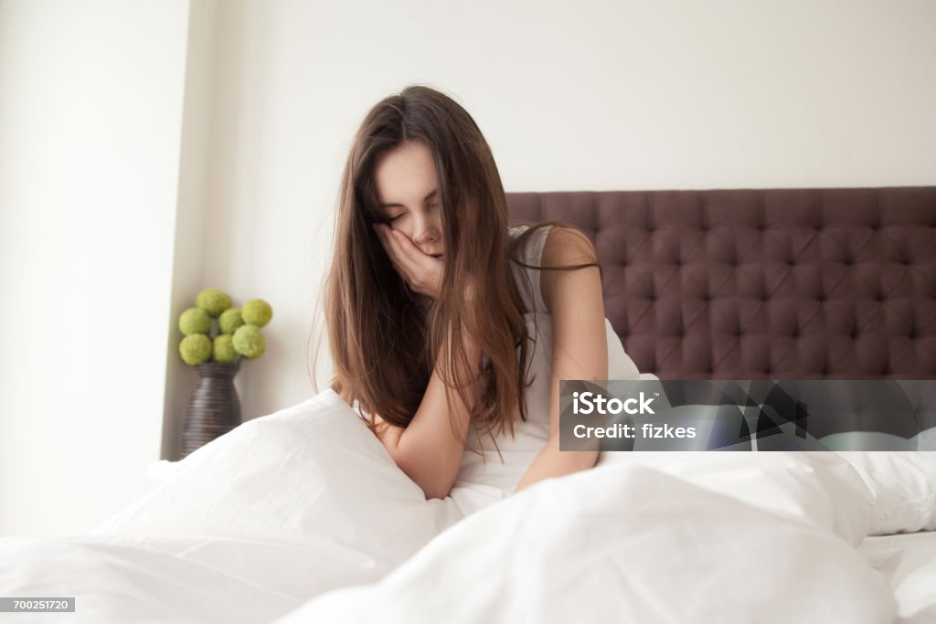 Agotada mujer sentada en la cama con el cabello desordenado - Foto de stock de Dormir libre de derechos
