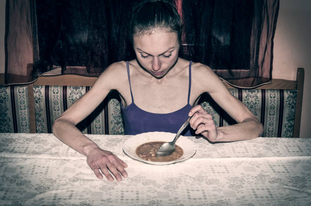 anorexia. skinny anorexic girl holding a spoon and look at the plate with food. - anorexia imagens e fotografias de stock