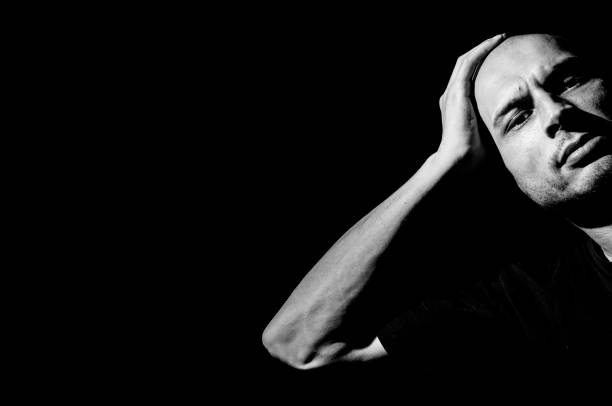 istock Angry man. Angry and frustrated man leaned his head on his hand. Dark background. Dark image. Black and white. 700271316