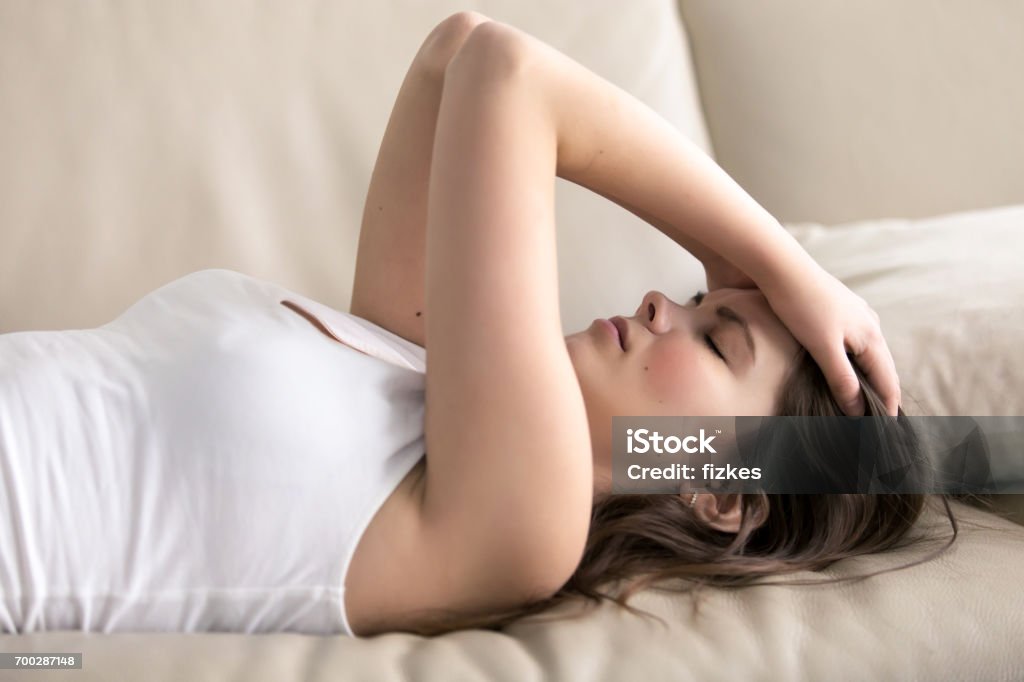 Young woman suffering of headache or migraine Woman lying on sofa having headache. Stressed girl suffering of fatigue, migraine, trying to cope with nervous tension, worries because of problems, unwanted pregnancy, negative thoughts and emotions Exhaustion Stock Photo