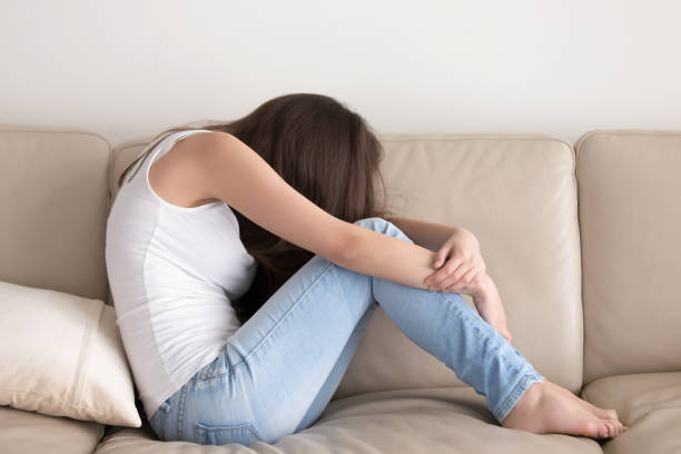 istock Depressed teen sitting on sofa and embracing knees 700287286