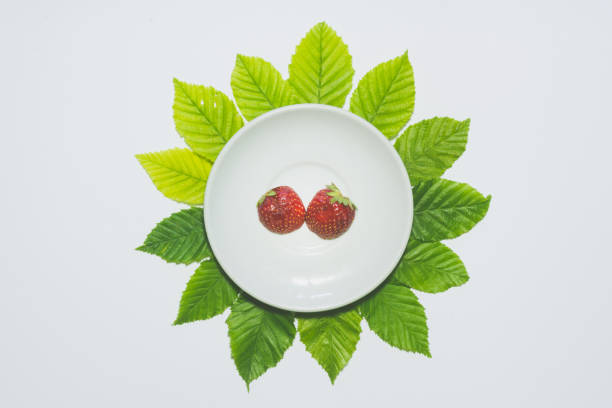 istock Minimal strawberry slice background. Fruit on white plate with leaves around it. Matte colored. 700313796