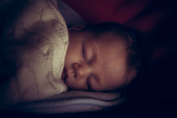 Newborn baby peaceful sleeping in dark room with low natural light covered with comfortable soft blanket symbolize peace and tranquility