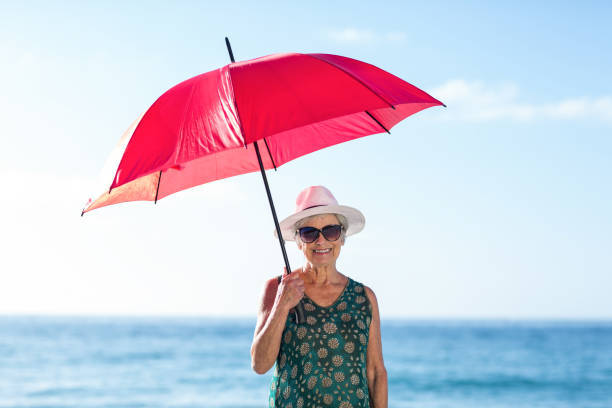 Senior woman posing with an umbrella at the beach