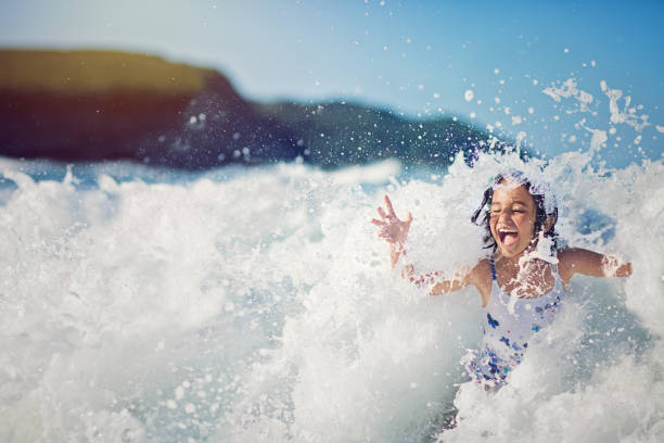 女の子をジャンプして大きな波で、海で遊んで - summer swimming beach vacations ストックフォトと画像