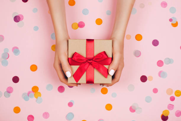 Hands holding present box Woman hands holding present box with red bow on pastel pink background with multicolored confetti. Flat lay style. birthday present photos stock pictures, royalty-free photos & images