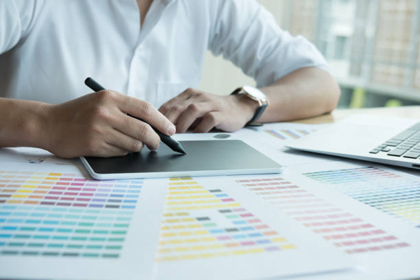 istock young graphic designer working with computer and color swatch. creative man using stylus pen and digital tablet at modern office. Architect using work tools and sample colour catalog. business, technology, design and people concept 700451132