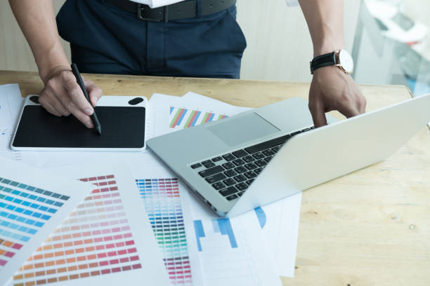istock young graphic designer working with computer and color swatch. creative man using stylus pen and digital tablet at modern office. Architect using work tools and sample colour catalog. business, technology, design and people concept 700451168