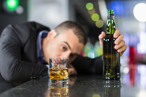 Drunk businessman slumped on bar beside drink